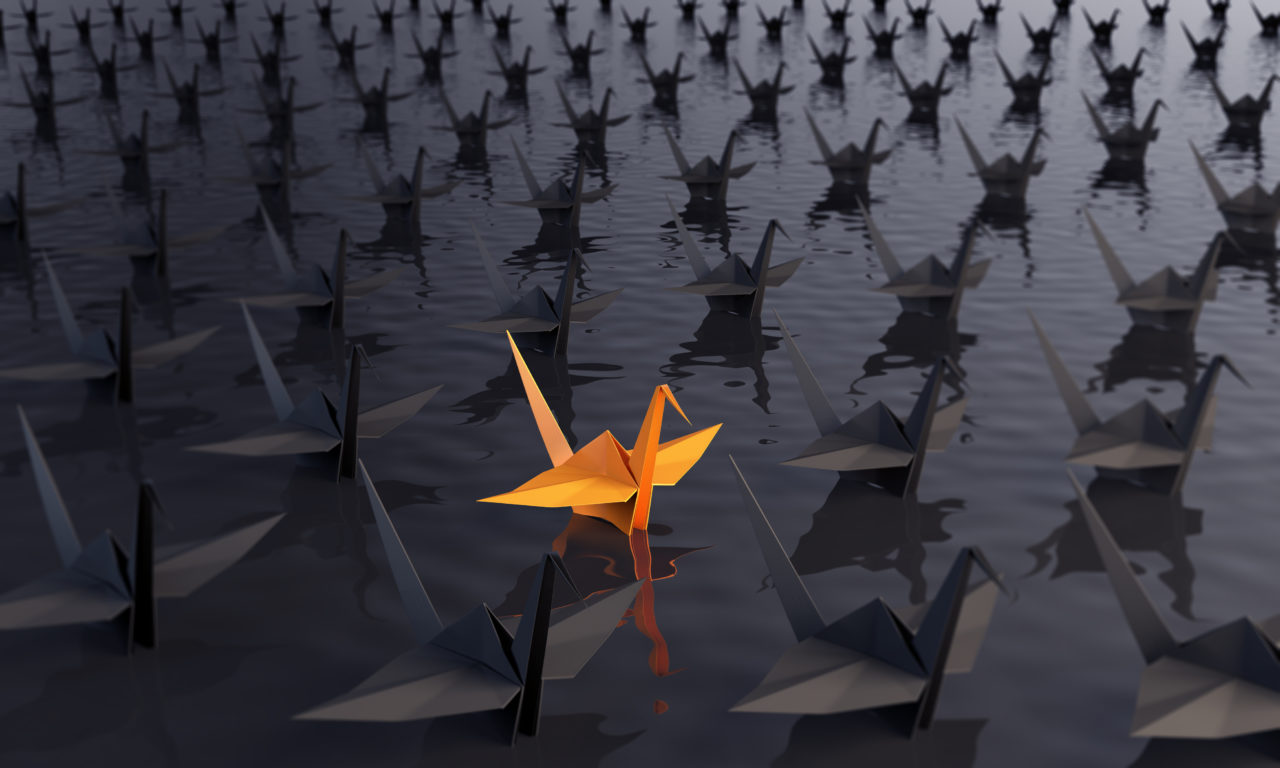 orange coloured origami swan stands out from the other black ones